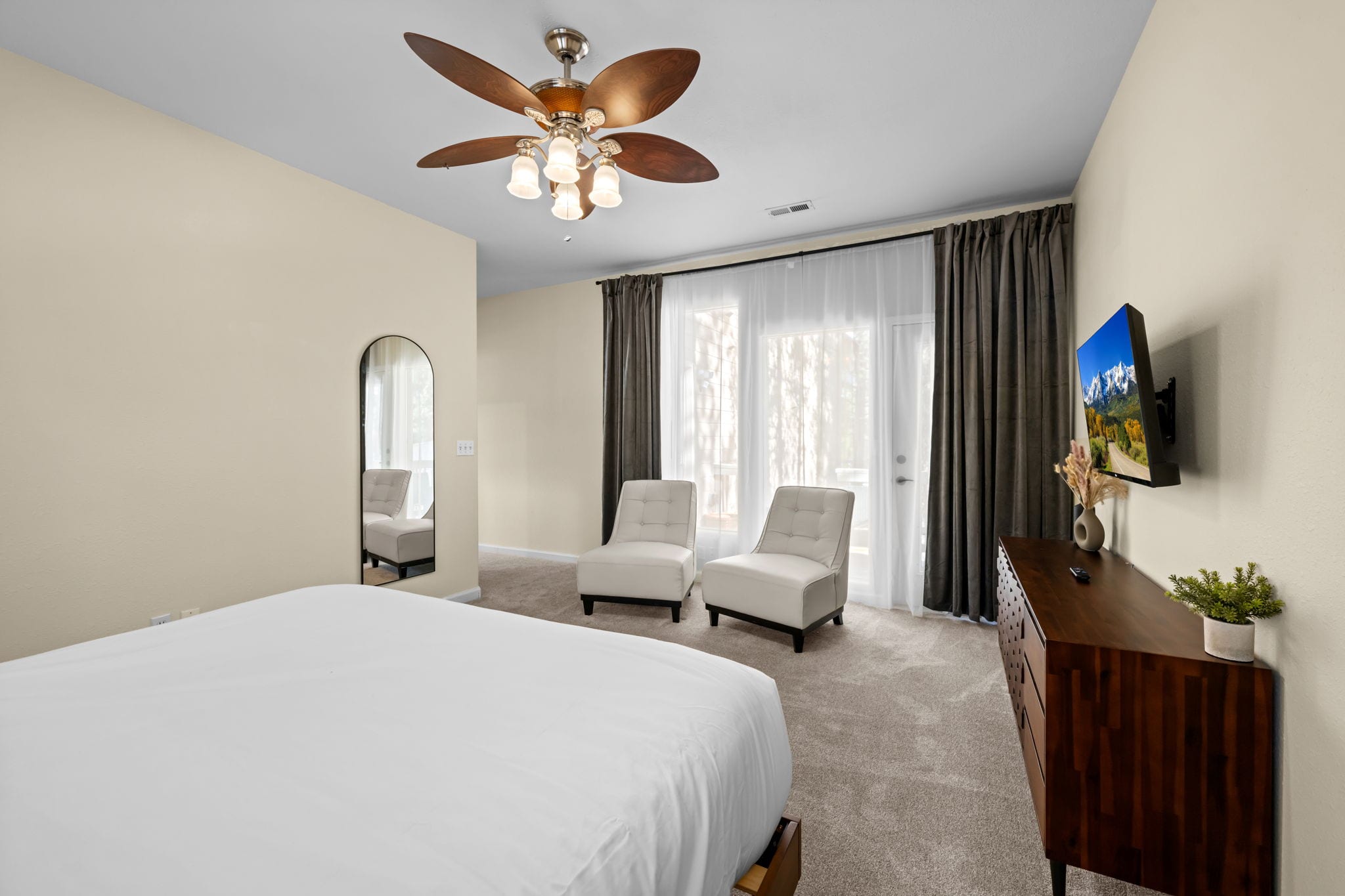 Bedroom with wooden bed frame, white bedding, two nightstands and a wall-mounted TV